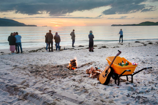 Young people gather on Balnakeil beach to celebrate the mid summer setting sun. Balnakeil,Northwest Scotland-July 28 2022: Folks traveling Scotland,enjoy the late sunset and warm mid-summer weather,socializing with beer,music and a campfire,on the fine sands of the remote bay. beach fire scotland stock pictures, royalty-free photos & images