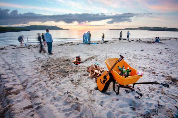 Young people gather on Balnakeil beach to celebrate the mid summer setting sun. Balnakeil,Northwest Scotland-July 28 2022: Folks traveling Scotland,enjoy the late sunset and warm mid-summer weather,socializing with beer,music and a campfire,on the fine sands of the remote bay. beach fire scotland stock pictures, royalty-free photos & images