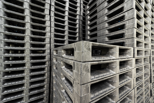 Tall stacks of heavy duty black plastic pallets in a factory.