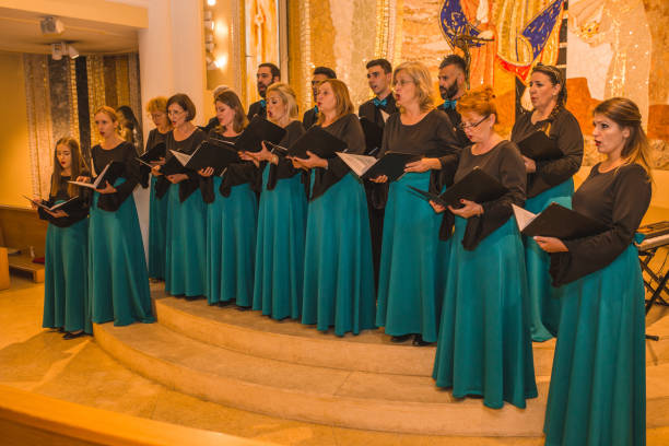 A group of people dressed in the same, formal clothes practicing before a choir performance