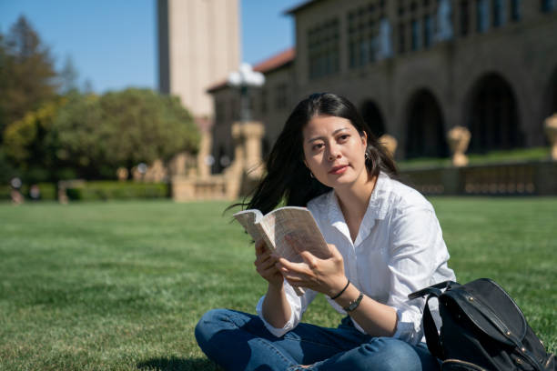 istock successful asian taiwanese woman school student looking into space with smile while reading a book on grass between classes on beautiful school campus on a sunny day 1439894779
