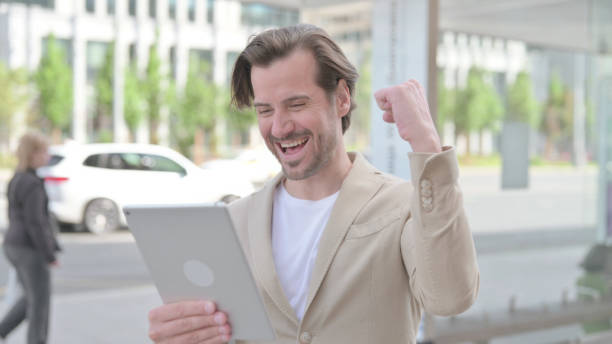 istock Young Man Celebrating Online Win on Tablet Outdoor 1439899058