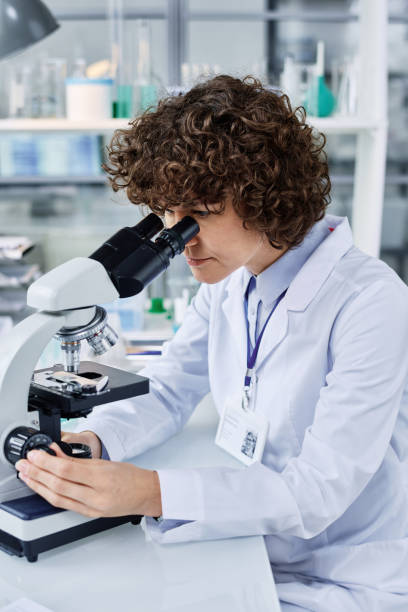 istock Young chemist or virologist in labcoat looking in microscope in laboratory 1439900246