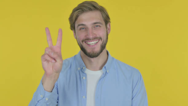 istock Young Man with Victory Sign on Yellow Background 1439900312