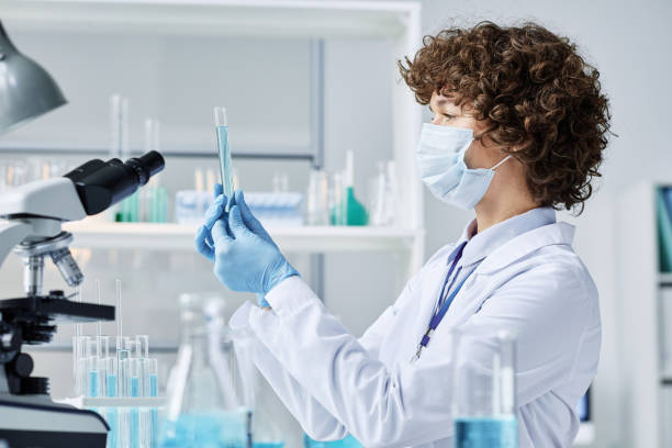 istock Young virologist in protective mask and gloves holding flask with blue liquid 1439900376