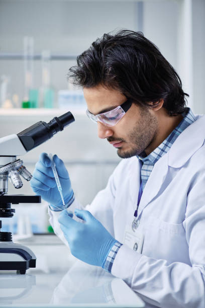 istock Young serious chemist in labcoat dropping liquid substance into petri dish 1439901344
