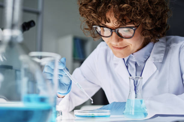 istock Young female scientist or chemist dropping liquid substance into petri dish 1439902382