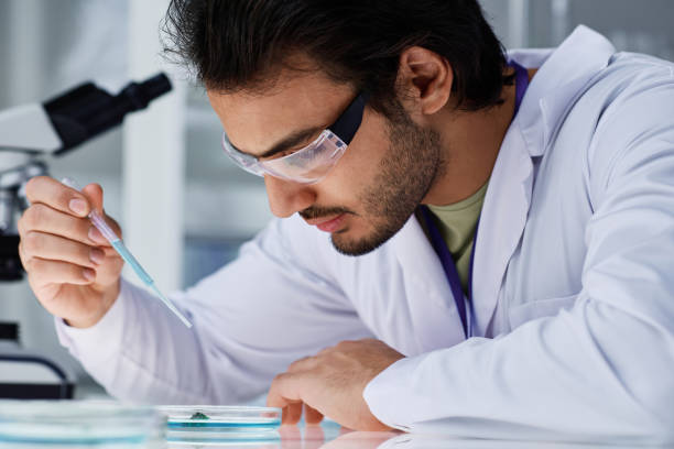 istock Young serious man in eyeglasses and labcoat dropping liquid substance 1439902472