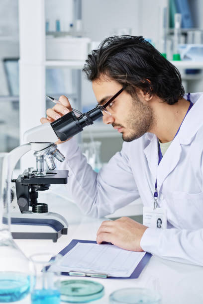 istock Serious clinician studying bacteria or new virus in microscope in laboratory 1439902473