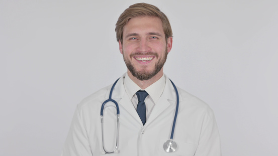 Portrait of hero in a white coat. Cheerful smiling young doctor with a stethoscope in a medical hospital standing against a white background. Coronavirus covid-19 danger alert. High quality photo