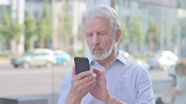 istock Old Man Browsing Internet on Smartphone Outdoor 1439905057