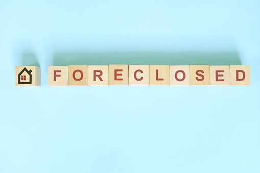 Foreclosed property concept in real estate. Wooden blocks typography on blue background.