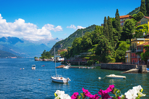 Enchanting view of Lake Como with fishing boats near the shore of Varenna, a charming medieval village in Lombardy, Italy, on a sunny summer day with the green Swiss mountains in the background.