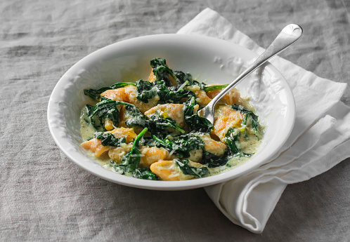 Pumpkin gnocchi with spinach cream sauce on a grey background, top view. Delicious lunch