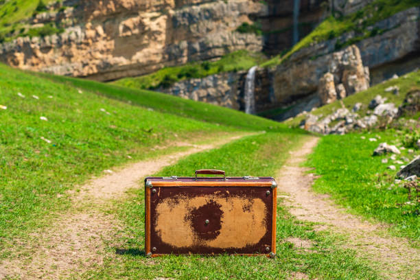 Old shabby leather suitcase on a dirt road in the mountains