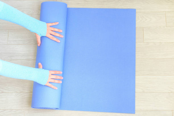 istock Female hands roll up rubber blue exercise mat on the floor close-up, top view. 1439910493