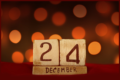 December 24 Christmas Eve vintage wooden block calendar on red fabric, festive bokeh lights background greeting card celebrating holidays, birthday, save the date for special occasion.