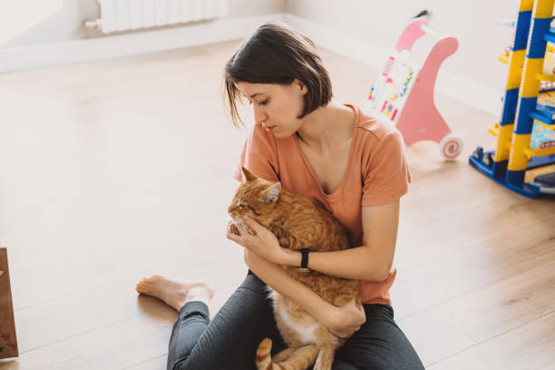 istock Young woman caressing fluffy kitten while resting on living room floor in summer day. Pets loving and caring concept. Positive person. 1439912089