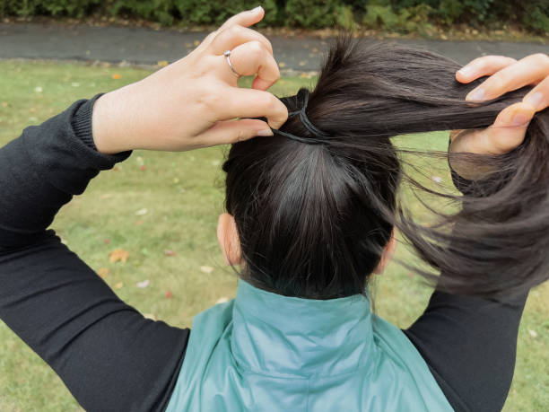 jeune femme multiraciale attachant ses cheveux en queue de cheval dans un parc - district of north vancouver photos et images de collection