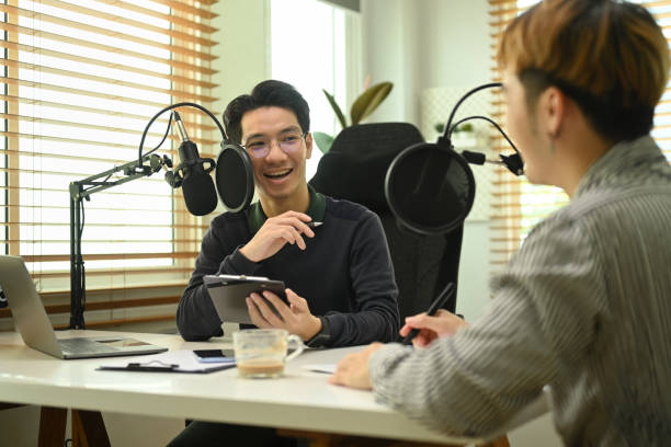 istock Two young asian male bloggers looking and talking each other while recording conversation, interview for their channel. 1439913326