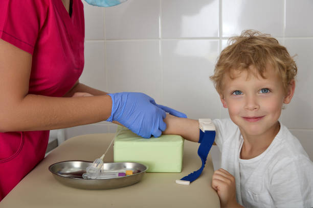 niño sonríe a la cámara mientras enfermera con túnica roja toma sangre para analizarla de la vena - naughty nurse fotografías e imágenes de stock