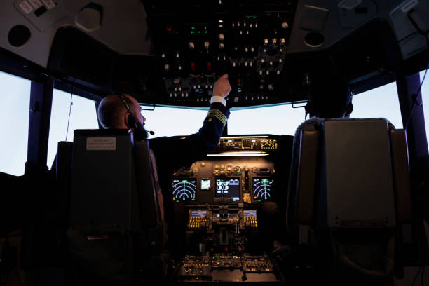 istock Male captain pushing dashboard buttons in plane cockpit 1439915849