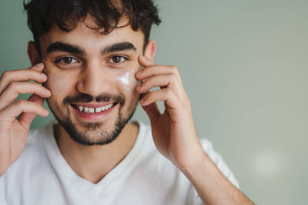 istock Young handsome caucasian smiling man applying moisturizing face cream on face isolated over green wall with copy space. Millennial guy caring about skin health and hydration. Skincare, dermatology, facial cosmetics concept. 1439915883