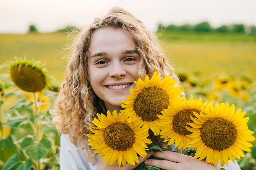 Happy farm girl embracing flowers in a field of blooming sunflowers. Colorful landscape. Nature summer. Natural beauty.
