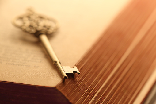 An old key rests in an open book. Photographed with a very shallow depth of field.