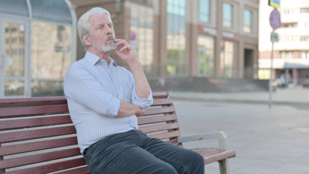 istock Pensive Old Man Thinking while Sitting Outdoor on Bench 1439916267