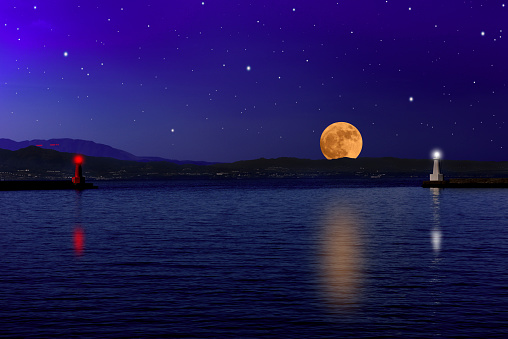 Full moon rising over the sea and the lighthouse with copy space.