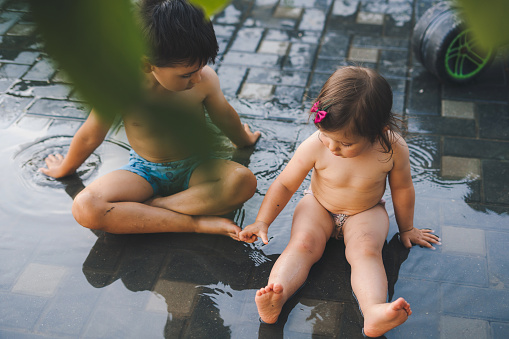 Two undressed children playing in the accumulated water after the rain, having fun outdoors in any weather. Summer evening. Outdoor fun by any weather