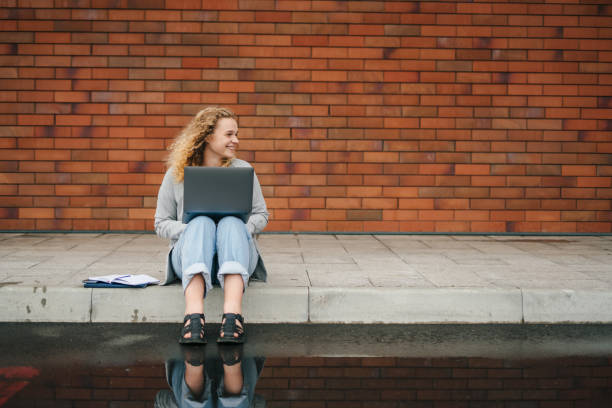 istock Full length young woman student writing note, studying and working online, outdoors sitting on the floor. Copy space. Distance education. 1439925584