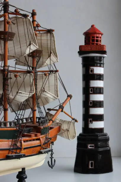 Toy Frigate With Fabric Sails Turned Bow To A Miniature Lighthouse Stock Photo