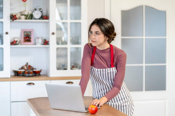 istock Young female baker sitting on kitchen counter typing on laptop 1439927560