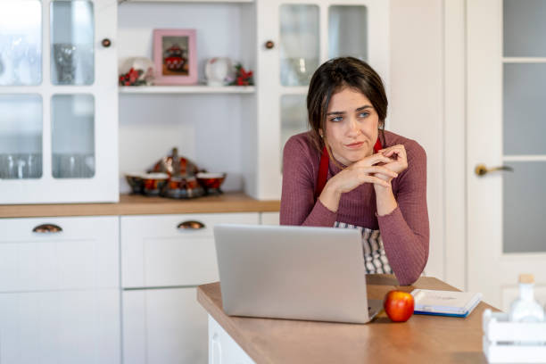 istock Young female baker sitting on kitchen counter typing on laptop 1439927561
