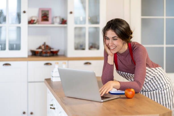 istock Young female baker sitting on kitchen counter typing on laptop 1439927562