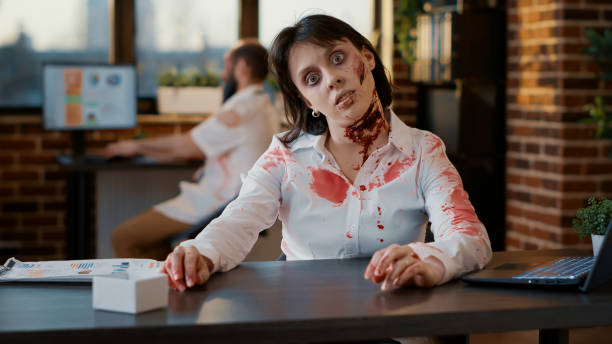 istock Ugly spooky looking walking dead person sitting in office while waving at camera. 1439929097