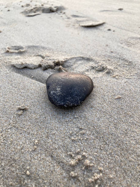 istock Smooth black stone on the sand at the beach 1439929706