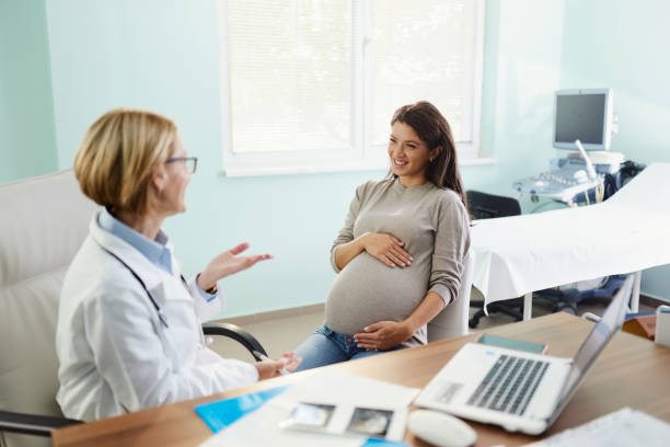 Happy pregnant woman talking to her gynecologist in the office. stock photo