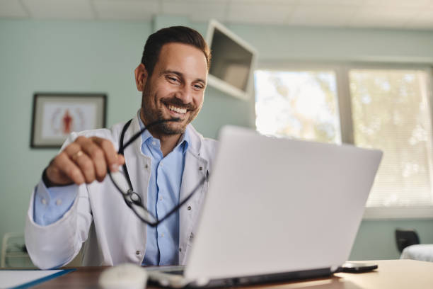 Happy doctor reading an e-mail on laptop in the office. stock photo