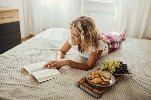 istock Relaxed woman reading a book during morning snack on a bed. 1439933221