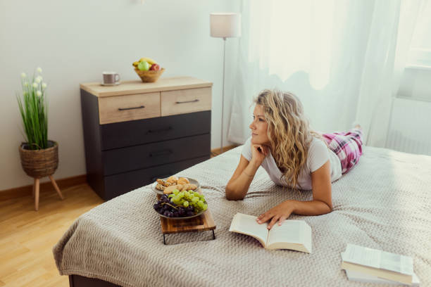 istock Pensive woman reading a book on a bed. 1439934056