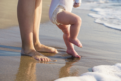 Baby walks on the sea beach and learns to walk with his mother. First steps, parental care and love concept. High quality photo