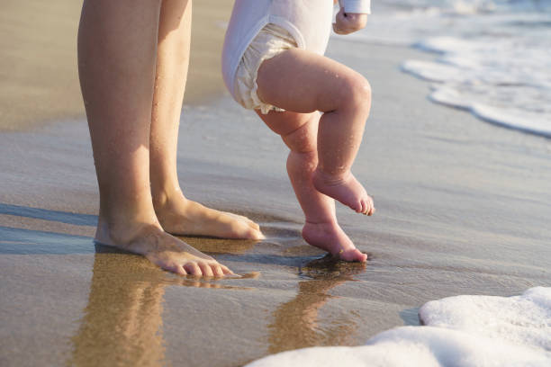 dziecko chodzi po plaży morskiej i uczy się chodzić z matką. pierwsze kroki, opieka rodzicielska i koncepcja miłości - baby toe zdjęcia i obrazy z banku zdjęć