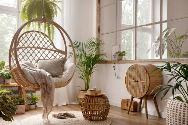 istock Creative composition of boho living room interior with hanging swing, rattan commode, plaid, beige pillows, round coffee table and personal accessories. Home decor. Template. 1439939445