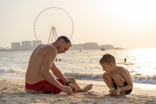 Father and son play on the beach against the backdrop of views of Dubai. International Father's Day