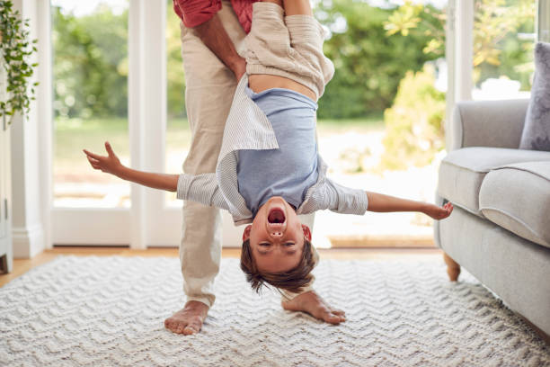 istock Father Holding Son Upside Down Playing Game In Lounge At Home Together 1439945740