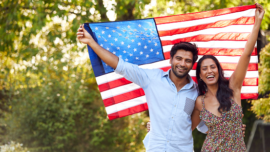 Portrait Of Patriotic American Couple Holding USA Stars And Stripes Flag Outdoors In Garden