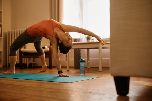 Asian female athlete stretching while doing backbend exercises while working out at home. Copy space.